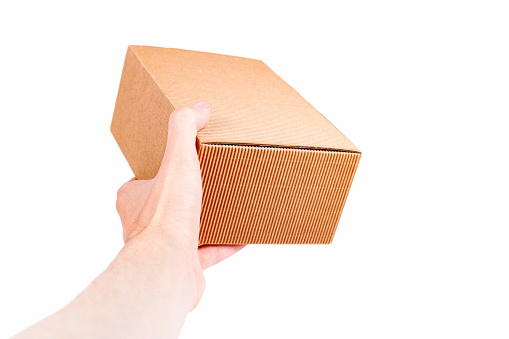 Man handing a small brown closed cardboard package, quick shipment delivery, transportation and product shipping concept first person view Carton box held in hand isolated on white post office courier