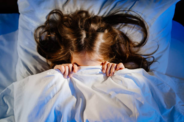 恐ろしい女の子は彼女の部屋のベッドで毛布で彼の顔を覆います。子供の恐怖 - child bedtime imagination dark ストックフォトと画像