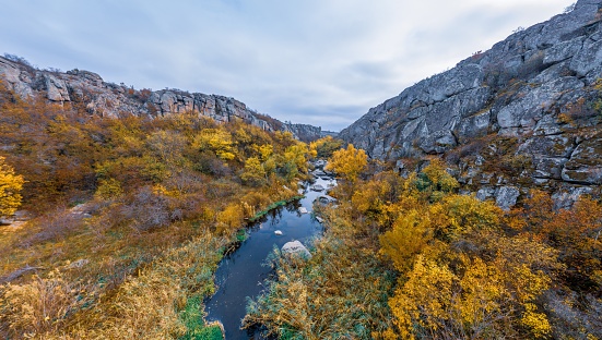A stream flows in the Aktovsky Canyon, Ukraine. Autumn trees and large stone boulders around. Aerial panoramic drone shot