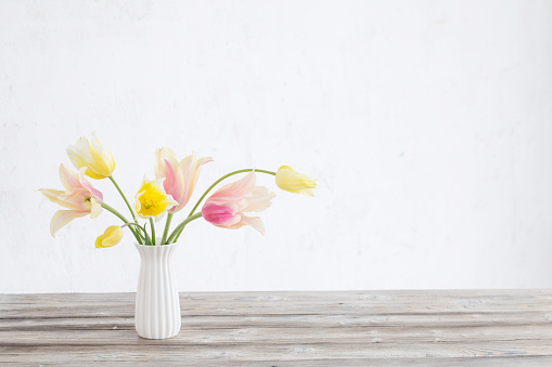 yellow and pink tulips in vase on background old white wall