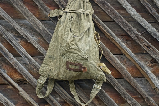 one old green army backpack duffel bag hanging on brown boards on the wall outside