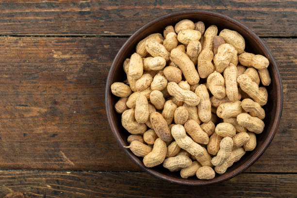 istock Unpeeled peanuts in a clay plate on a white wooden table. 1291004274