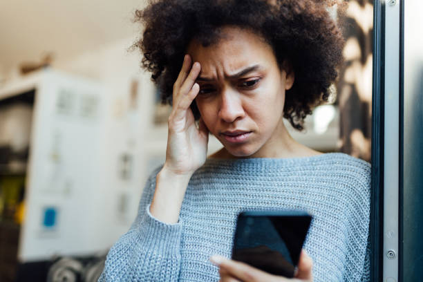 彼女のモバイルデバイス上で悪いニュースを読んで若いアフリカ系アメリカ人の女性 - frustration emotional stress surprise women ストックフォトと画像