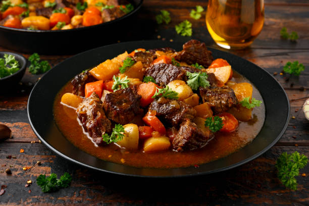 estofado de ternera con zanahoria y patata bebé en plato negro sobre mesa de madera - beef stew fotografías e imágenes de stock