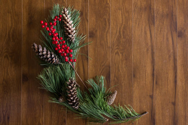 Christmas and New Year background with fir branches, holly and cones on brown wooden background, top view