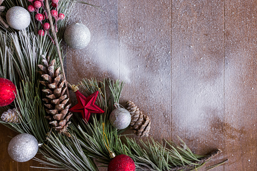 Christmas and New Year background with fir branches, holly, Christmas ornaments and cones on brown wooden background, top view