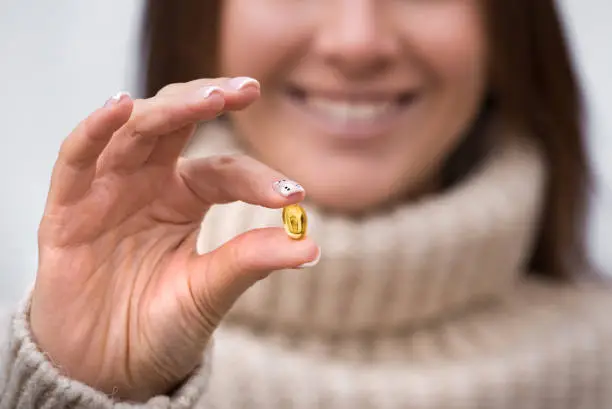 Smiling woman holding fish oil pill or vitamin D supplement. Taking capsule with omega 3 or D3. Vitamin and dietary supplements. Healthy diet nutrition. High quality photo