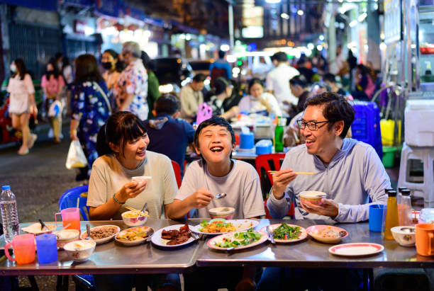 아시아 가족이 방콕 야오와라트 로드에서 많은 사람들과 함께 길거리 음식 레스토랑에서 음식을 먹는 것을 즐깁니다. - bangkok night thailand traffic 뉴스 사진 이미지