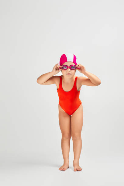 little child girl in swimsuit, swimming goggles and swim cap. Full length little child girl in swimsuit, swimming goggles and swim cap is preparing for swimmin. Full length. child dreams of becoming a swimming champion swimming cap stock pictures, royalty-free photos & images