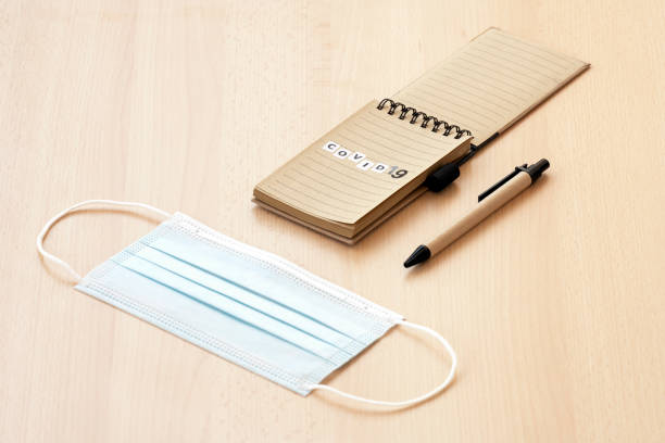 istock Flat lay with copy space. A face mask, a spiral notepad with “Covid-19” written on it and a pen are arranged on a wooden table. 1291025077
