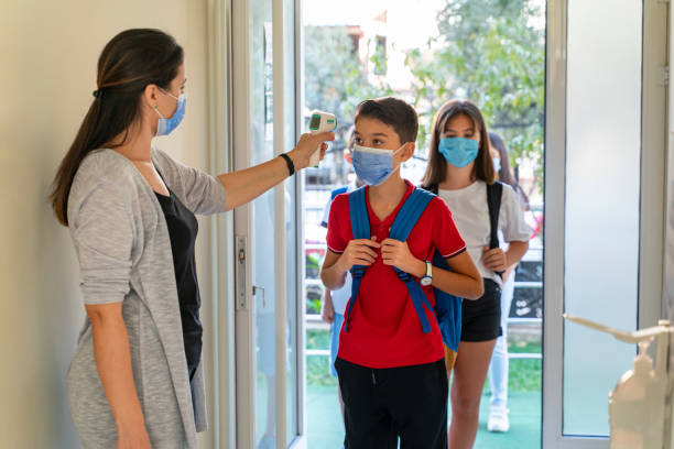 istock Teacher checking temperature of students with face mask for pandemic while children go back to school 1291025872