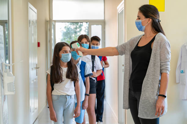 istock Teacher checking temperature of students with face mask for pandemic while children go back to schoolv 1291026178