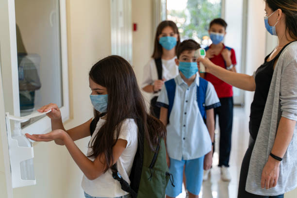 lehrer überprüft temperatur von schülern mit gesichtsmaske auf pandemie, während kinder wieder zur schule gehenv - control clothing image technique image type stock-fotos und bilder