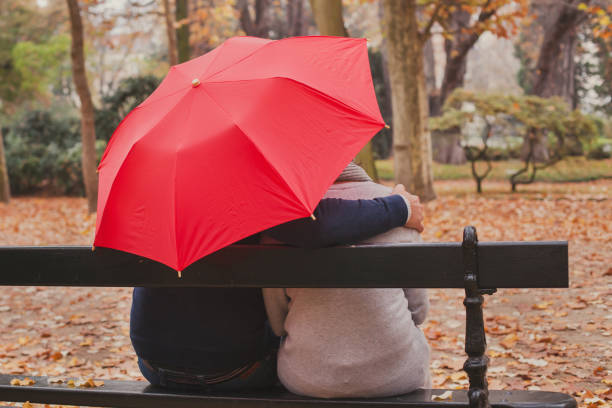 comforting and psychological support, care concept, man hugs woman under umbrella - solicitous imagens e fotografias de stock