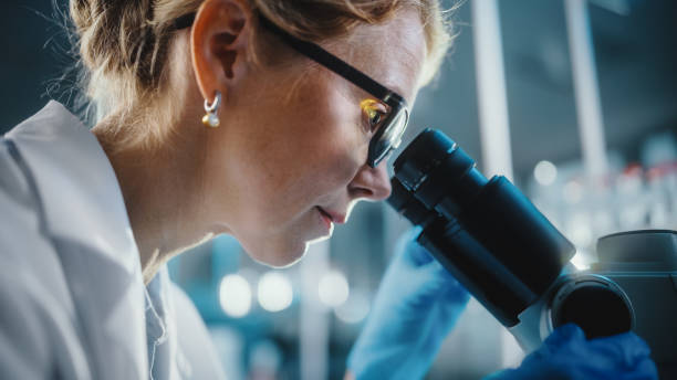 dans bright medical science laboratory: beautiful microbiologist wearing glasses looks under microscope analyze sample. brilliant scientist, docteur, travaillant avec high-tech equipment. plan rapproché tiré - drug discovery photos et images de collection