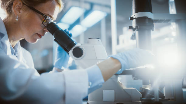 istock Bright Medical Science Laboratory: Beautiful Microbiologist Looks Under Microscope Does Analysis of Test Sample. Brilliant Scientist, Doctor, working with High-Tech Equipment. Close-up with Sun Flare. 1291031197
