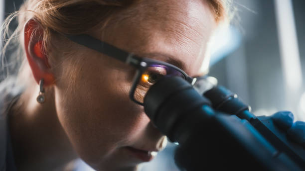 istock In Bright Medical Science Laboratory: Beautiful Microbiologist Wearing Glasses Looks Under Microscope Analyzing Sample. Brilliant Scientist, working with High-Tech Equipment. Macro Close-up Shot 1291031209