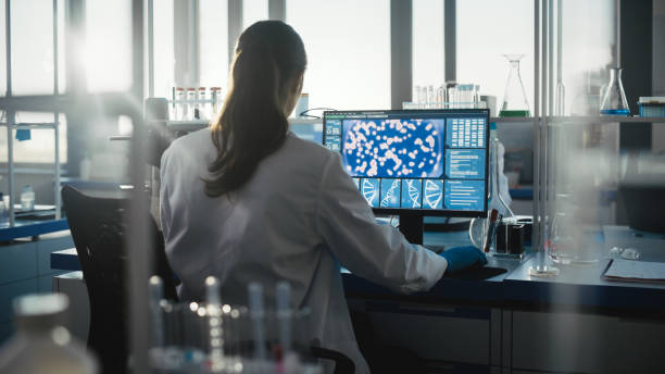 laboratorio di scienze mediche con diversi team di scienziati biotecnologici professionisti che sviluppano farmaci, biochimica femminile che lavora sull'interfaccia di terapia genica che mostra il computer. scatto in visualizzazione posteriore - genetic research foto e immagini stock