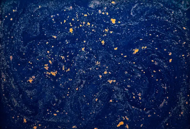 Gold paint powder floating on blue colored water.