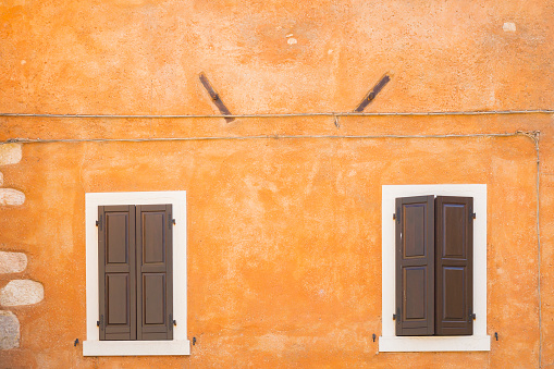Old orange house facade, closed brown window shutters in popular touristic historic village Garda, Italy