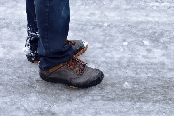 Photo of Man Wearing Sneakers and Blue Jeans Walking Outside on Icy Sidewalk