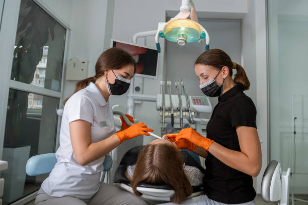 odontóloga con un asistente examina los dientes del paciente en la clínica - medical exam dentist dentists chair dental assistant fotografías e imágenes de stock