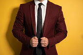 No head close up shot pf a hands holding a business man burgundy color jacket with two hands fixing it on a body isolated on yellow background