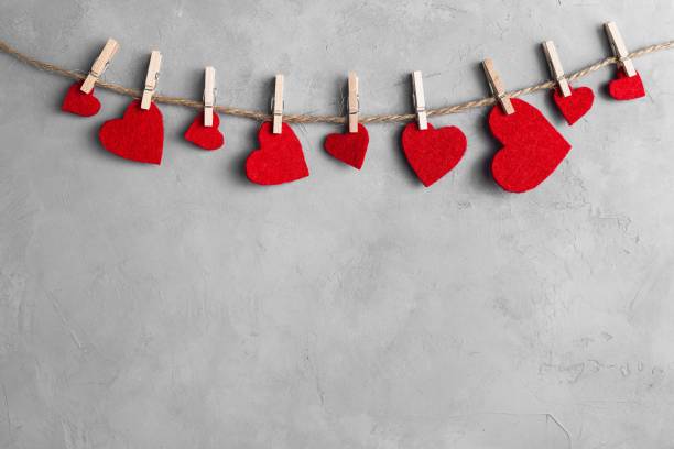 Red hearts on rope with clothespins, on a white grey concrete background. Place for text, copy space.