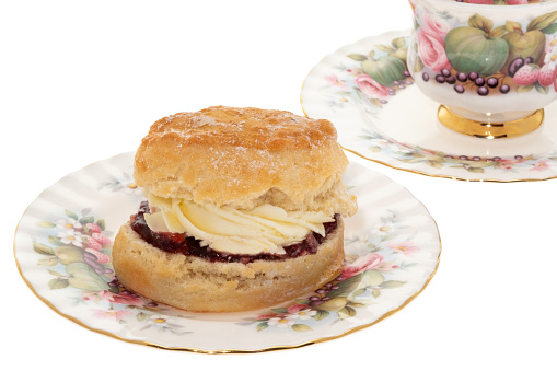 Fresh scone with whipped cream and strawberry jam placed on ornate antique crockery - white background