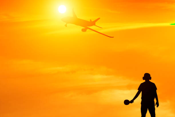 Photo of Silhouette of ground staff sending airplane taking off flight with orange sky background and lens flare effect