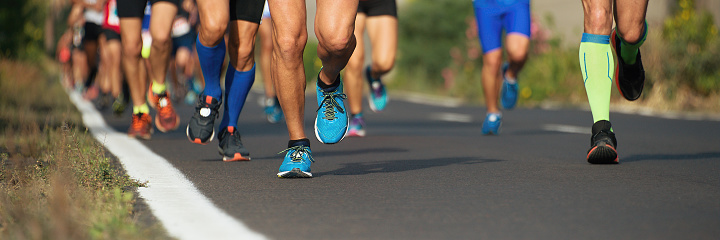 group of athletes running on asphalt street during marathon race, only legs with sport shoes