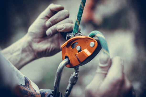 mains de l’homme fonctionnant un dispositif de belaying d’escalade - climbing mountain climbing rock climbing moving up photos et images de collection