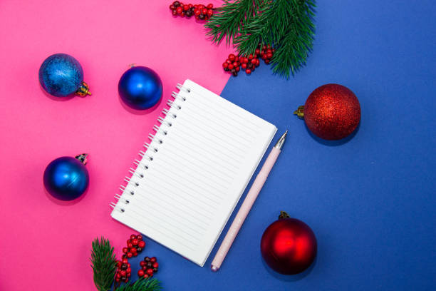 istock Christmas-tree decorations balls, Christmas tree branches and a notebook for writing on a blue background. The concept of recording Christmas and New Year greetings. Flat lay, top view 1291052363