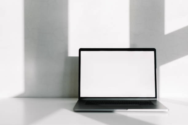 istock Laptop with white blank screen on the white table with shadow from window. 1291053633