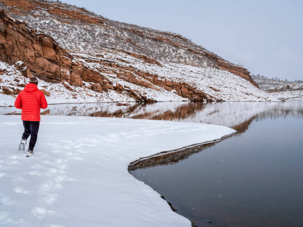 warm gekleideter mann joggt in der winterlandschaft am seeufer - fort collins reservoir lake water stock-fotos und bilder