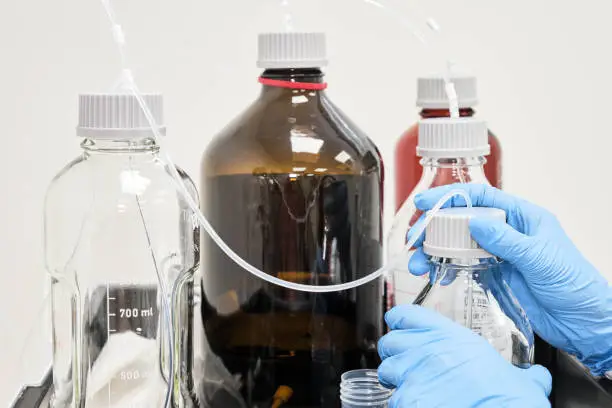 Photo of Close up womans hand changing a mobile phase solution in HPLC system. High performance liquid chromatography at clinical or analytical laboratory. Separation of organic compound, checking of purity of pharmaceuticals