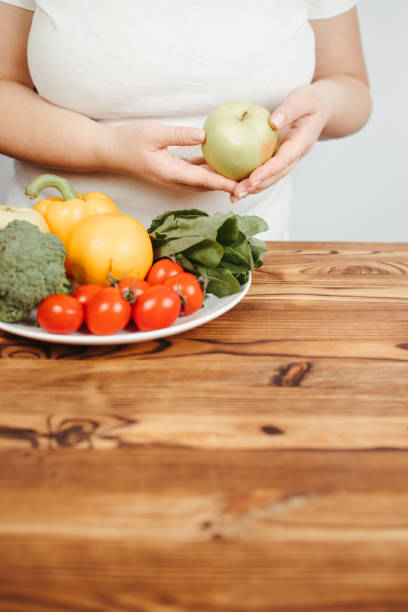 istock Fat woman snacking with fruits and vegetables 1291062928