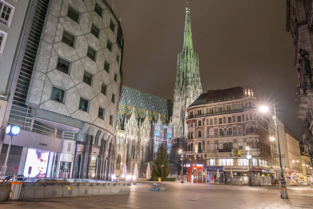 The empty "Stock Im Eisen" square in Vienna's 1st district during lockdown. VIENNA, AUSTRIA - DECEMBER 7, 2020 - The post modernist style Haas House on the left is designed by Hans Hollein and hosts the fashion store Zara on the ground floor. During the lockdown in December only pharmacies, banks, post offices, hospitals and supermarkets are allowed to stay open. St. Stephens Cathedral is illuminated at night and still welcomes visitors. city street consumerism window display vienna stock pictures, royalty-free photos & images