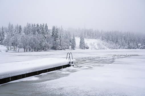 First snow of the winter and half frozen lake with bathing jetty in the hills above Oslo