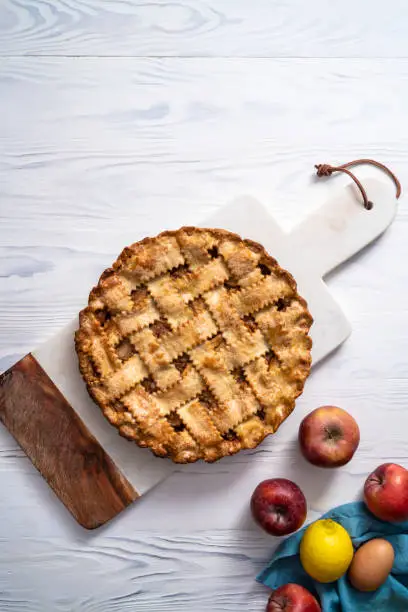 American apple pie on cutting board with ingredients on white wooden board table