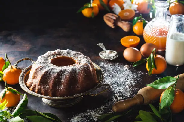 Bundt cake made of tangerine clementines baked homemade with ingredients on moody dark background