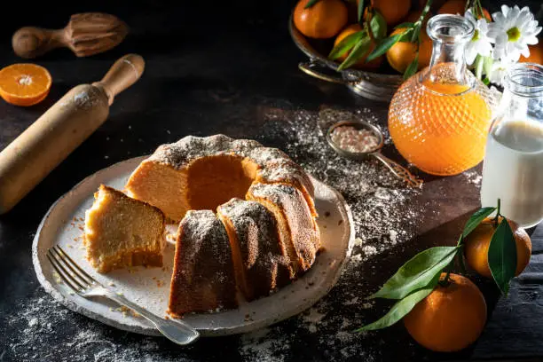 Bundt cake made of tangerine clementines baked homemade with ingredients on moody dark background