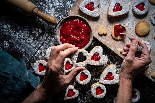 Linzer cookies biscuits food preparation with strawberry jam man hands with spoon homemade Bakery heart shape