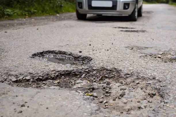 Photo of Road in terrible condition with many potholes and bumps and a car moving along it