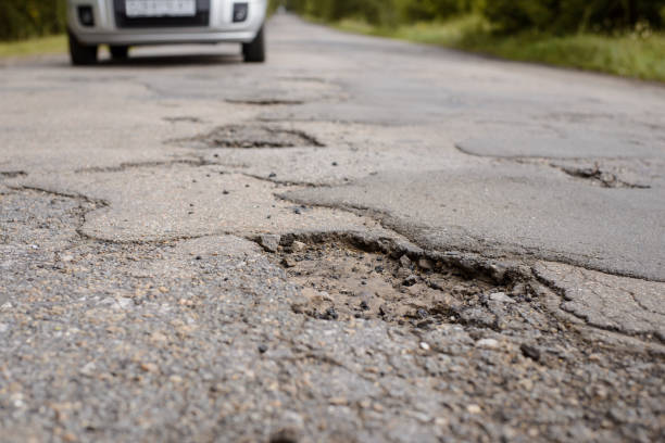 istock Damaged road and approaching car on the background 1291070674