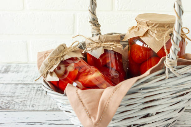 los tomates caseros se conservan en frascos de vidrio en cesta de mimbre blanco sobre fondo de madera - basket wicker marinated preserves fotografías e imágenes de stock