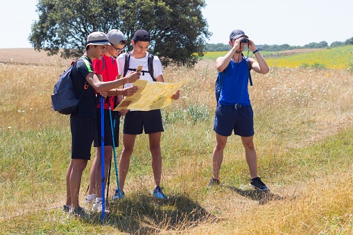 young people with trekking poles doing the Way of Saint James in Spain reading the map to get their bearings observing with binoculars and also looking for the location in the mobile phone of the place in a summer day