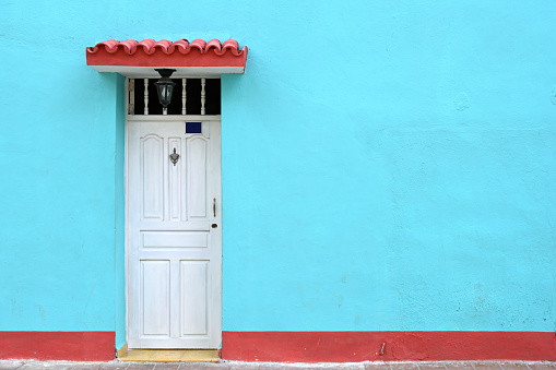 Front view of colorful, run-down residential building facade with vibrant turquoise and red color with white door in Havana, Habana, Cuba