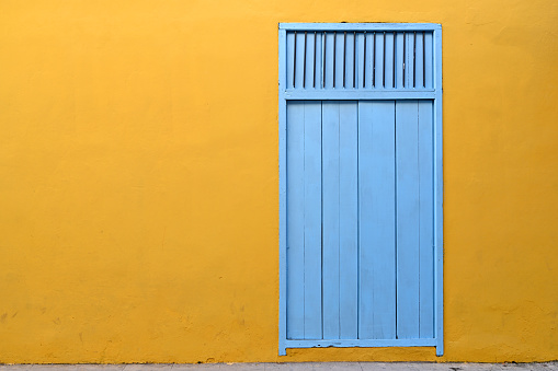 Front view of yellow colored, run-down building facade with vibrant turquoise door in Havana, Habana, Cuba