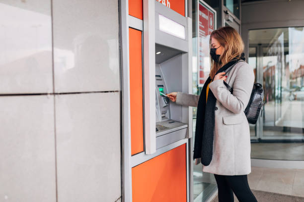 istock Woman using her credit card to withdraw money from ATM machine while wearing protective face mask 1291074295